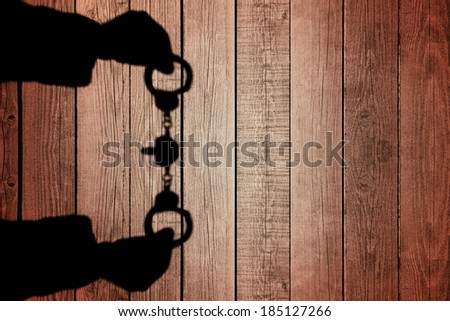 Human Hands Shadow with Handcuffs on Natural Wooden Background. You can see more silhouettes and shadows on my page.