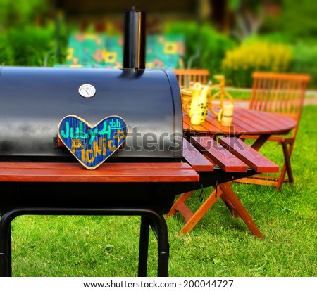 BBQ Summer Backyard Party Scene with sign JULY 4 th PICNIC on wooden heart. Tilt-Shift effect on background.