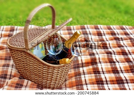 Picnic blanket and basket in the grass. Champagne  wine and glasses in the basket.