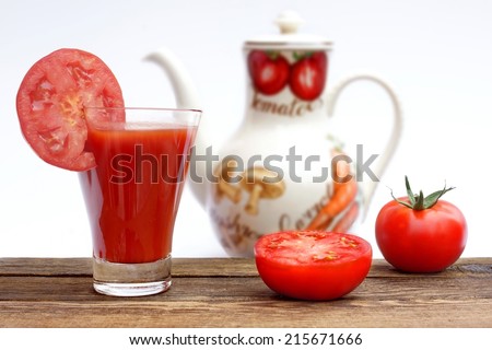 Tomato Juice on wooden board and two tomatoes. Blurred white jug  with Juice in the background.
