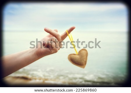 Woman Hand with Fabric Heart Hanging which Flying in the Wind. Sea Water in the background