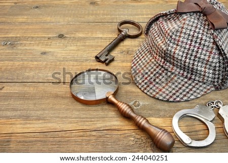 Sherlock Holmes Cap famous as Deerstalker, Old Key, Real Handcuffs and Vintage Magnifying Glass on Grunge Wooden Table