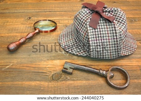 Sherlock Holmes Cap famous as Deerstalker, Old Key and Retro Magnifier on Grunge Wooden Table