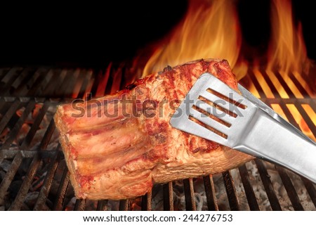 Tongs Holding Grilled Pork Ribs. Hot Flaming BBQ Grill on the Background
