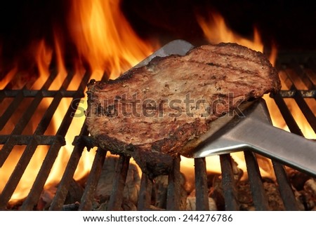 Spatula with Beef Steak on the Grill. Flames of Fire on the Background.