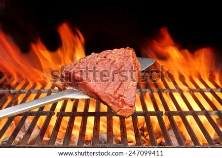 Raw Beefsteak on the Blade Over a Hot BBQ Grill. Flames of Fire on the Black Background.