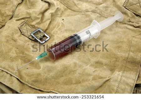 Medical Syringe With Brown Liquid on Camouflage Army Bag or Military Fabric Background