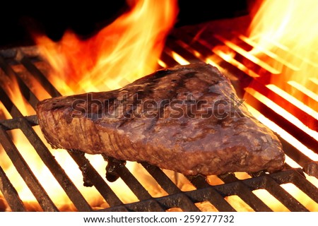 Marinated Beef Steak On The Hot BBQ Charcoal Grill. Flame Of Fire In The Background.