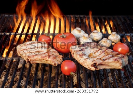 Two Tasty Rib Steaks, Vegetables, Tomato, Mushrooms Cooked Over Flaming Hot BBQ Grill. Summer Cookout or BBQ Party or Picnic Scene With Nobody. Black Background Isolated.