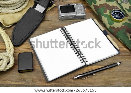 Preparing For Travel Concept. Open Empty Notebook With White Pages, Compact Digital Camera, Rope, Compass, Pen, Pencil, Hunting Knife,  Bag, Cigarette Lighter On Grunge Wood Table Background