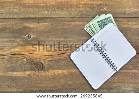 Open Notebook With Checkered White Pages and One USA Dollar Bills On Grunge Wood  Textured Background With Copy Space For Text or Image. Overhead View