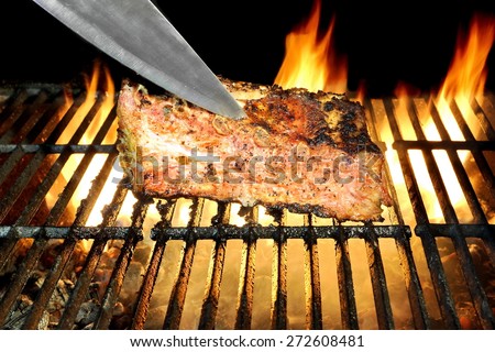 Pork Ribs Chop And Chief Knife  On The Hot Flaming BBQ Grill, Flames of Fire On The Black Background