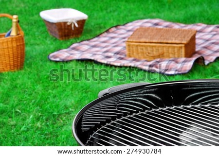 Barbecue Grill On The Lawn Picnic Basket With Food And Wine, Blanket On The Emerald Spring Grass Background