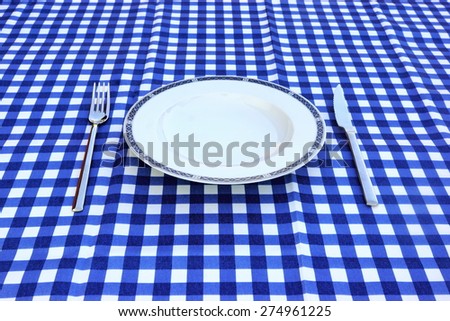 Empty White Plate, Knife And Fork On The Checkered Blue White Picnic Tablecloth Background