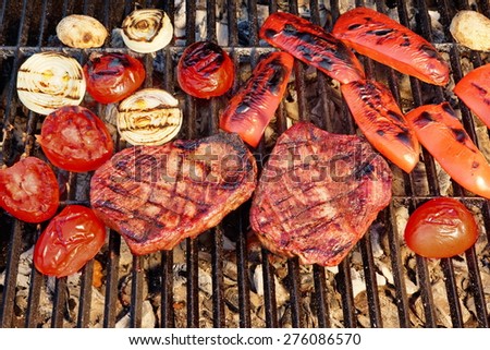 Two Flame Broiled Beef Steaks And Vegetables On BBQ Grill Close-up. Good Food For Outdoor Summer Barbecue Party Or Picnic