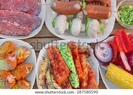 Wood Table With Different Cookout Food For Summer BBQ Grill Family Picnic Party. Beef Steaks, Mushrooms, Corn Cob, Onion, Sausages, Chicken Legs, Bell Pepper, Carrot, Potato, Kebabs, zucchini