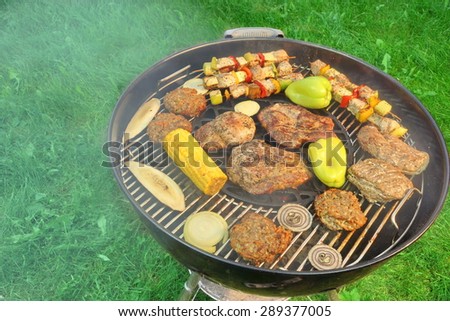 BBQ Charcoal Kettle Hot  Grill With Smoke, Steaks, Kebabs And Vegetables On The Summer Backyard Lawn Background Top View