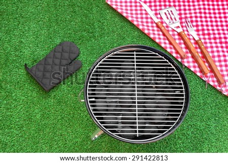 Summer Weekend Or Holiday BBQ Grill Party Or Picnic Concept. Park Or Backyard Fresh Lawn In the Background. Portable Kettle Charcoal Grill And Tools Close-up