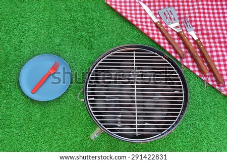 Weekend BBQ Grill Picnic Concept Overhead View On The Kettle Charcoal Grill And Disposable Plastic Plate.  Summer Fresh lawn In The Background