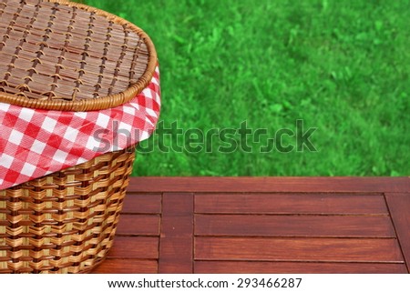 Picnic Basket On The Outdoor Rustic Wood Table Closeup, Bright Summer Green Grass In The Background