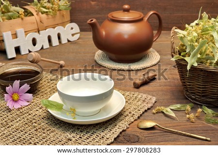 Home Tea Time Scene. Tea Cup With Lime Tree Herbal Green Tea, Honey, Herbs Leafs In The Basket, Clay Teapot, Vintage Spoon And Sign Home On Rustic Old Wooden Table