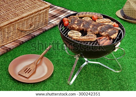 Summer Weekend Picnic Conceptual Scene On The Lawn With BBQ And Grill. Hamper, Blanket and Hat In The Background. Grill And BBQ Food Close-up.