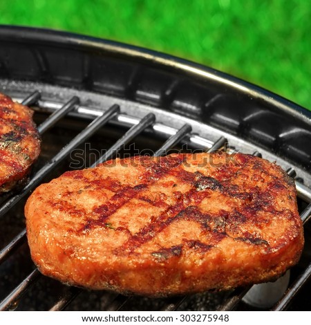 Close-up Of BBQ Hamburger Patties On The Hot Portable Charcoal Grill. Backyard Grass In The Background. Cookout Food For Summer Weekend Picnic Or Party.