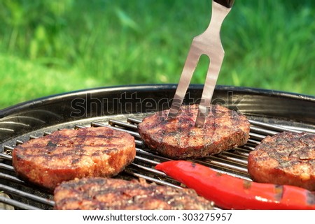 Close-up Of BBQ Hamburger Patties, Chili Pepper And Fork On The Hot Charcoal Grill. Backyard Lawn In The Background. Cookout Food For Summer Weekend Picnic Or Party.