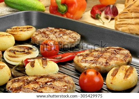 Homemade pan-fried burgers, pepper and grilled potato balls in the hot grill-pan on rustic dinning table. Hamburgers Ingredients in the background. Rustic Food Still-life
