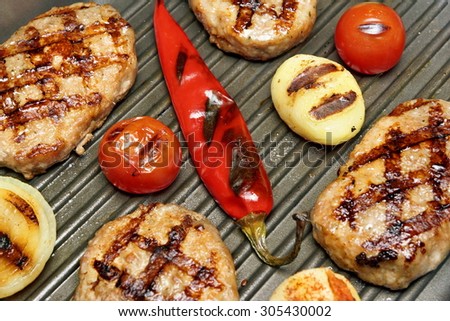 Close-up of hot homemade pan-fried burgers, potato, tomato and chili pepper in the grill-pan. Top View
