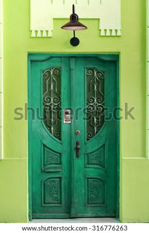 House Wall Fragment With Retro Green Wooden Door And Old Hanging Lamp, Carved Door Have Intercom System And Window With Lattice