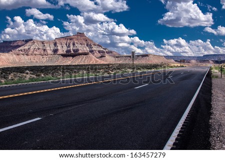Road in Utah under a blue sky with small clouds and the typical Utah mountains
