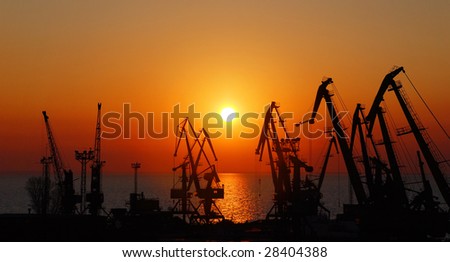 Silhouettes of port cranes on a background of a rising sun.