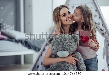 Attractive young woman with little cute girl are having fun together at home. Mom and daughter are sitting on the floor, hugging, kissing and smiling. Happy family concept. Mother\'s day.