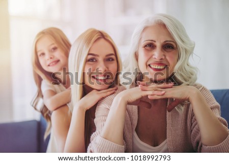 Little cute girl, her attractive young mother and charming grandmother are spending time together at home. Women\'s generation. Happy International Women\'s Day!