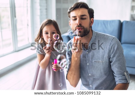 I love you, dad! Handsome young man at home with his little cute girl are having fun and blowing soap bubbles. Happy Father\'s Day!