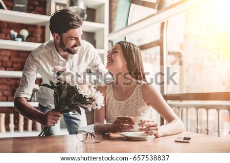 Surprise! Beautiful romantic couple in cafe. Young man is presenting flowers to his beloved. Feel of happiness.