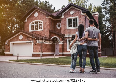 Back view of happy family is standing near their modern house and hugging