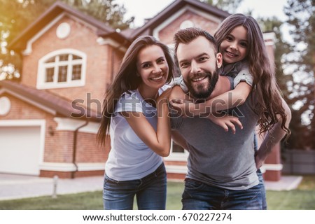 Happy family is standing near their modern house, smiling and looking at camera.