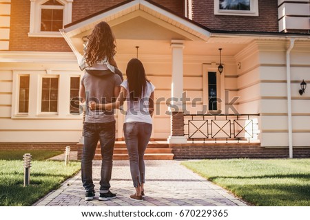 Back view of happy family is standing near their modern house.