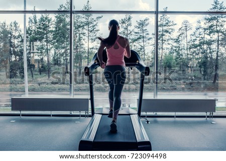 Attractive young sports woman is working out in gym. Doing cardio training on treadmill. Running on treadmill.