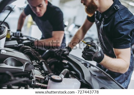 Cropped image of two handsome mechanics in uniform are working in auto service. Car repair and maintenance. Checking the oil level.