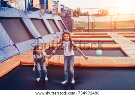 Little pretty girls having fun outdoor. Jumping on trampoline in children zone. \
Amusement park