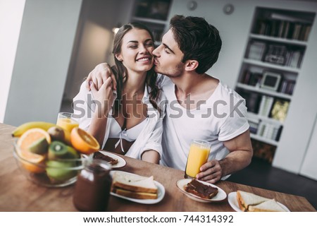 Good morning! Young romantic couple is having breakfast on modern light kitchen. Sexy woman in underwear and men\'s shirt eating sandwiches and toasts, drinking orange juice. Healthy lifestyle concept.
