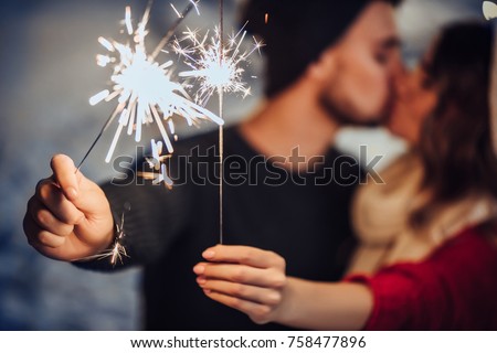 Young romantic couple is having fun outdoors in winter before Christmas with Bengal lights. Enjoying spending time together in New Year Eve. Two lovers are hugging and kissing in Saint Valentine's Day