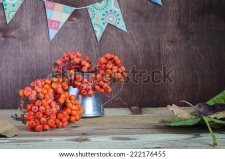 bunches of rowan in a pitcher on a background garlands of flags autumn still life