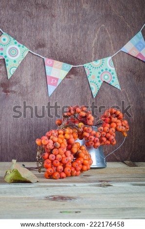 bunches of rowan in a pitcher on a background garlands of flags autumn still life
