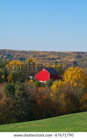 Vertical image of a bright red barn surrounded by autumn trees and a clear blue sky with room for copy