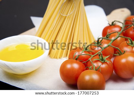 Italian pasta, spaghetti, cherry tomatoes and olive oil, on a wooden cutting board