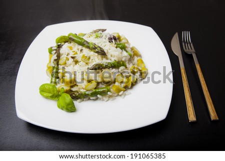 asparagus risotto on a white plate, dark background with blue glass and tableware